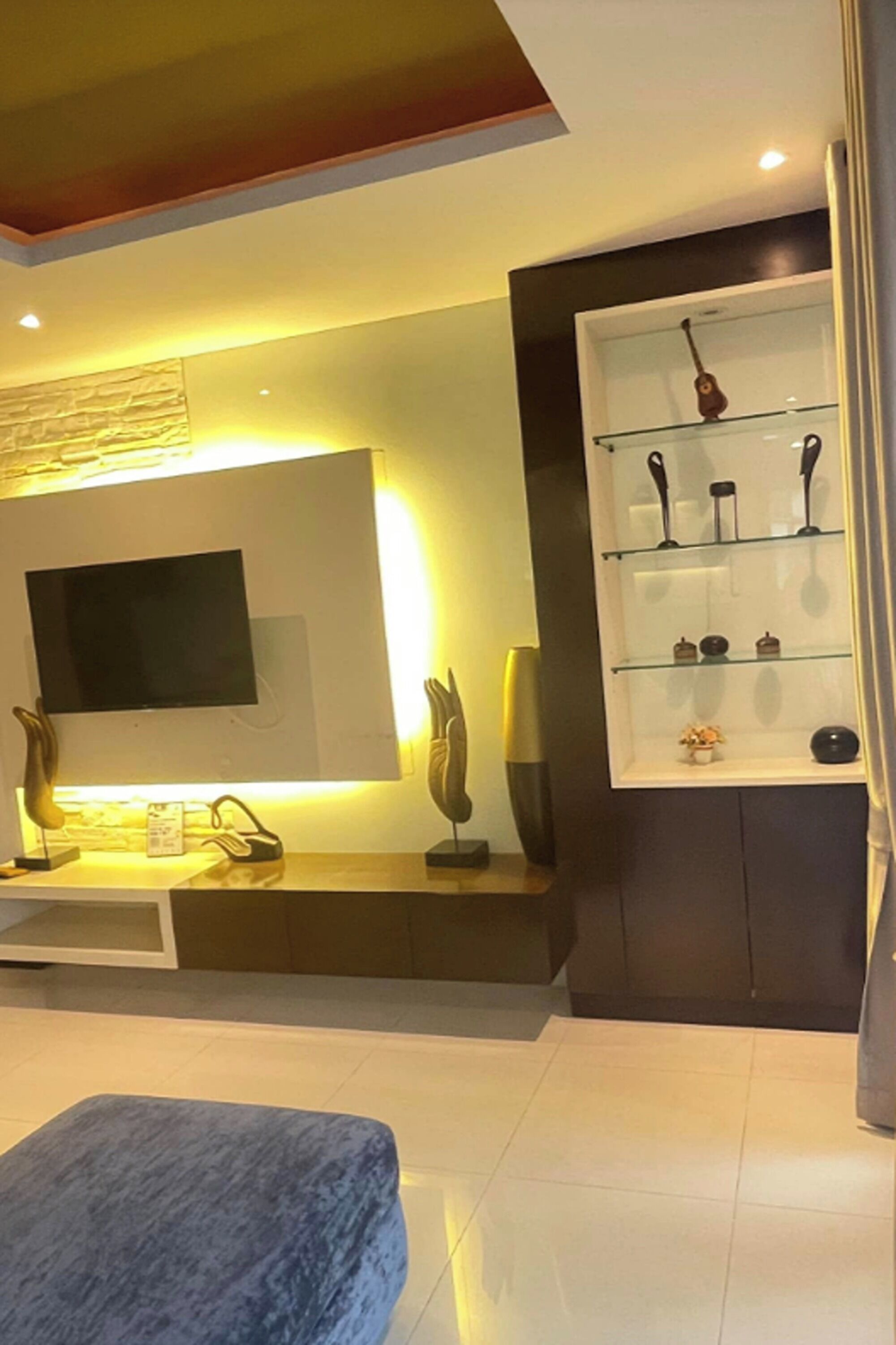 Een moderne woonkamer met een flatscreen televisie, een glazen displayplank en een blauwe poef.