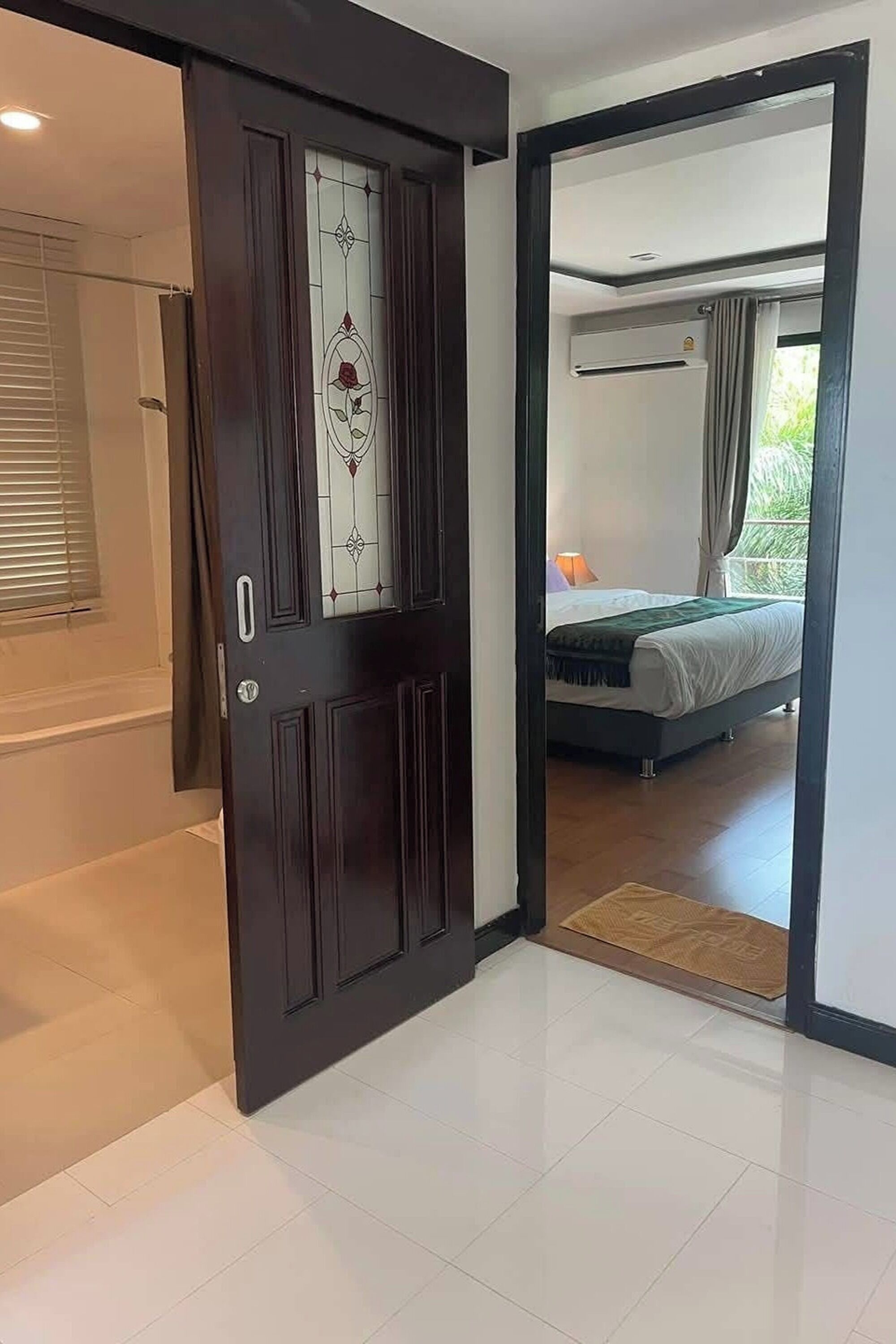 Ein Hotelzimmer mit einem Bett, einem Fenster mit Vorhängen und einer Tür zu einem weiteren Raum.