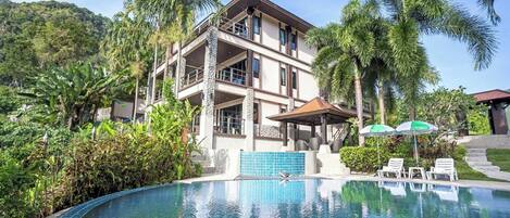 A multi-story hotel with a swimming pool, surrounded by lush greenery and palm trees.