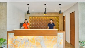 A reception desk with two staff members, a patterned wall, and pendant lighting. - Ginger Vadodara RCR (Vadodara)