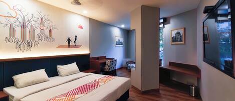 A modern hotel room with a large bed, a wall mural, a seating area, and a TV.