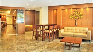 A modern lobby with a marble floor, wooden furniture, a sofa, and a decorative wall piece. - Ginger Vadodara RCR (Vadodara)
