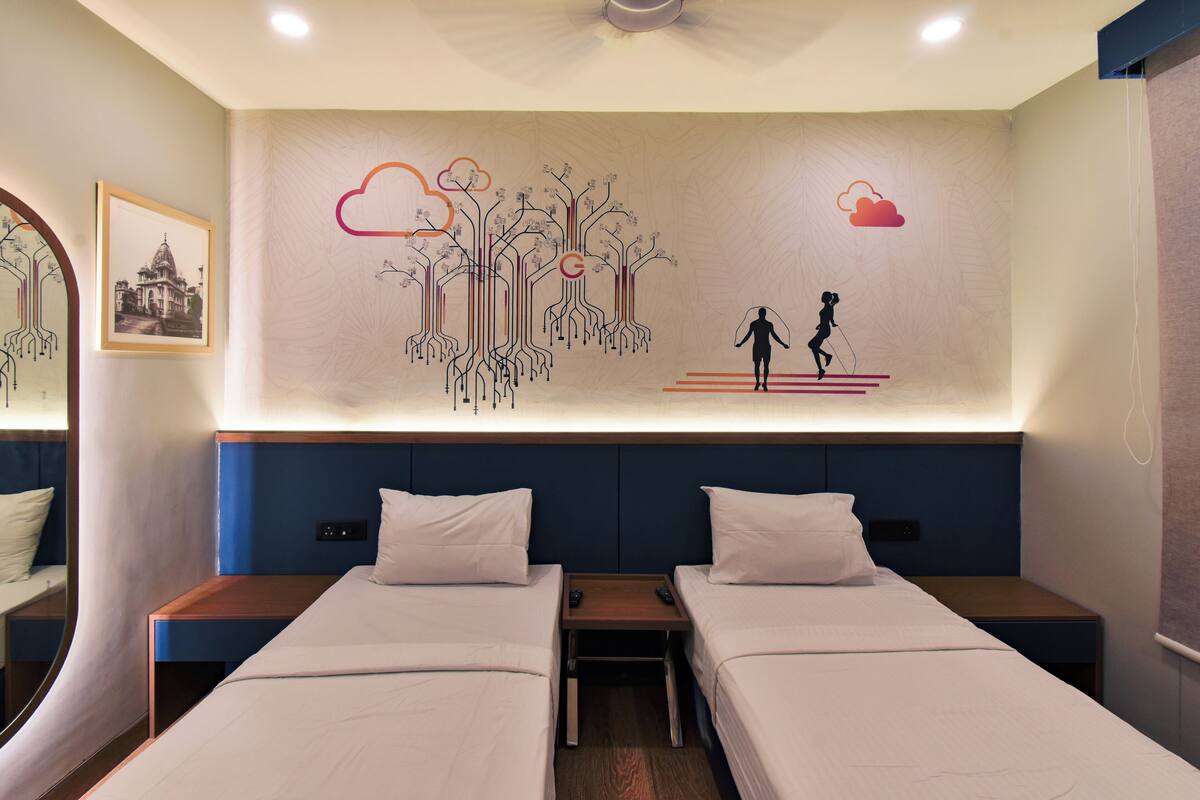 A hotel room with two beds, a nightstand, a wall-mounted artwork, and a framed picture.