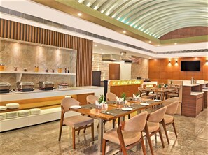 Un restaurante moderno con un área de comedor central, un bufé con diversas opciones de comida y una zona de cocina.