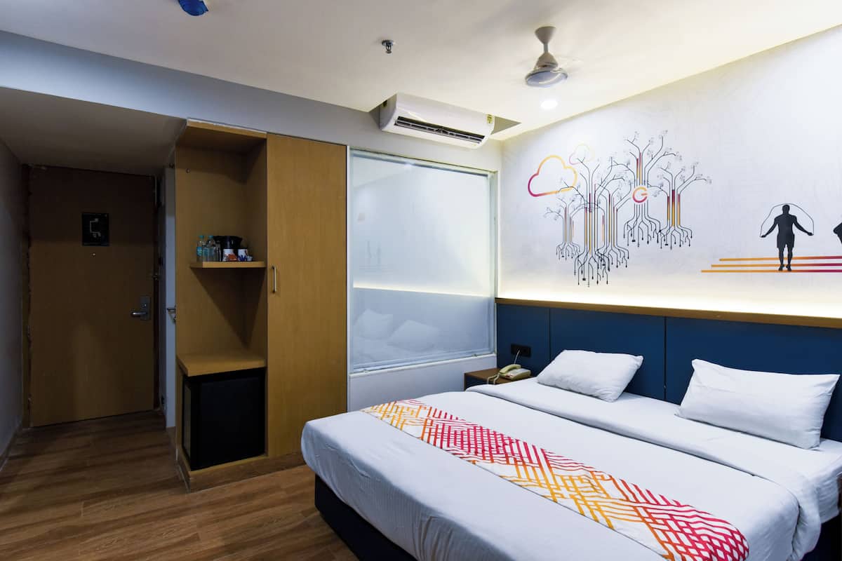 A hotel room with a bed, a wardrobe, a bedside table, and a wall with a graphic design.