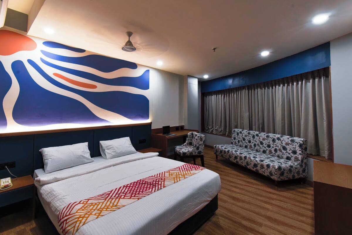 A hotel room with a large bed, a sofa, a desk, and a wall with abstract art.