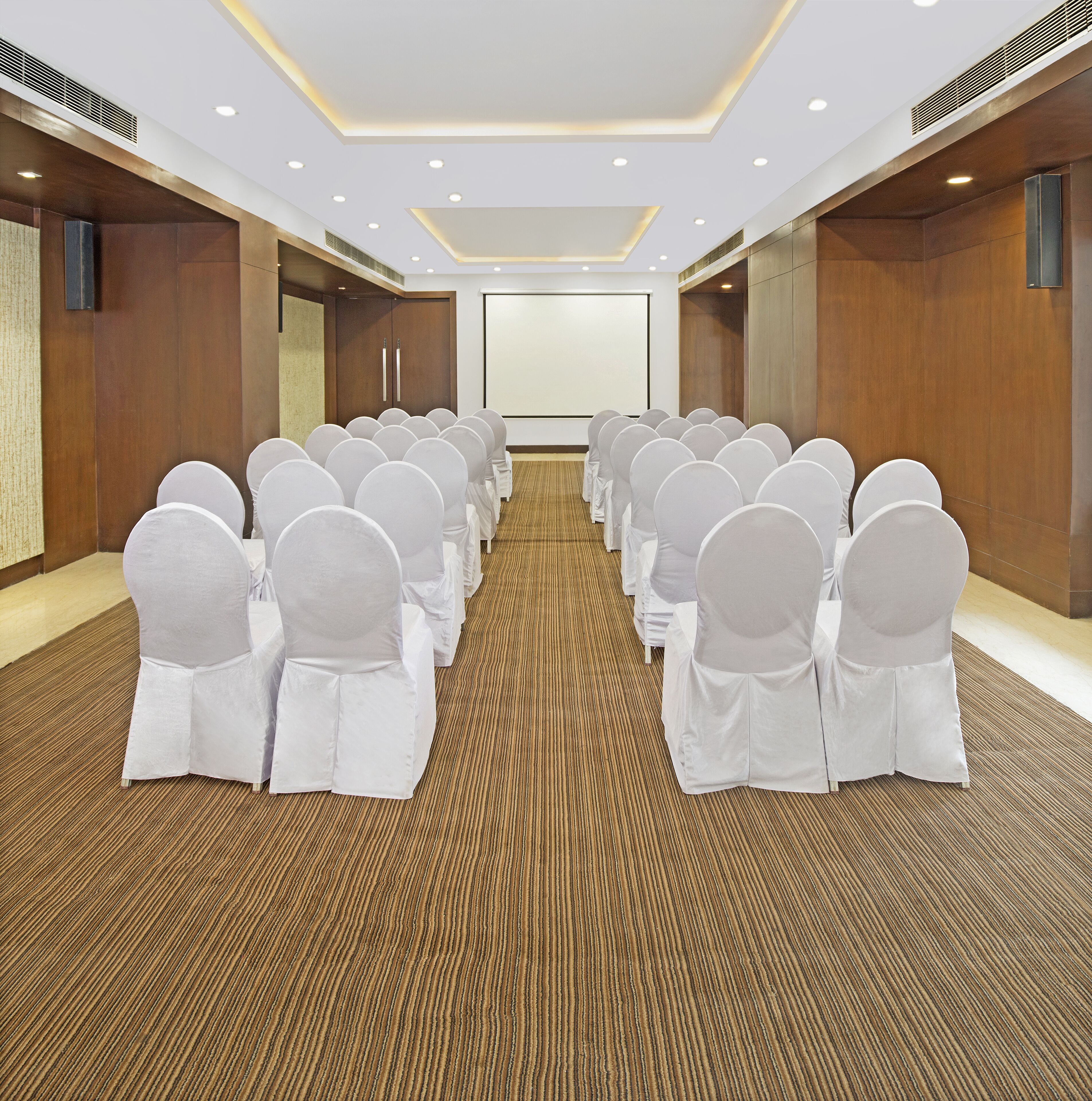 A conference room with rows of chairs, a projector screen, and a wooden floor.