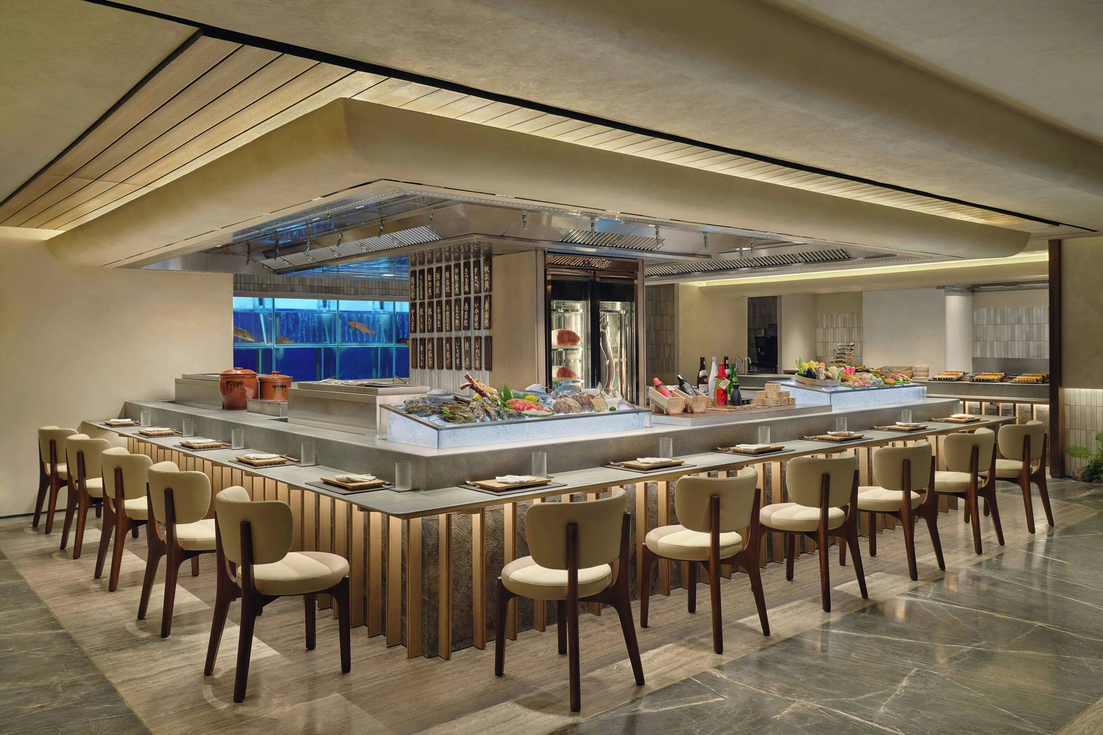 Un moderno bar con una barra larga, varios asientos y un acuario al fondo.