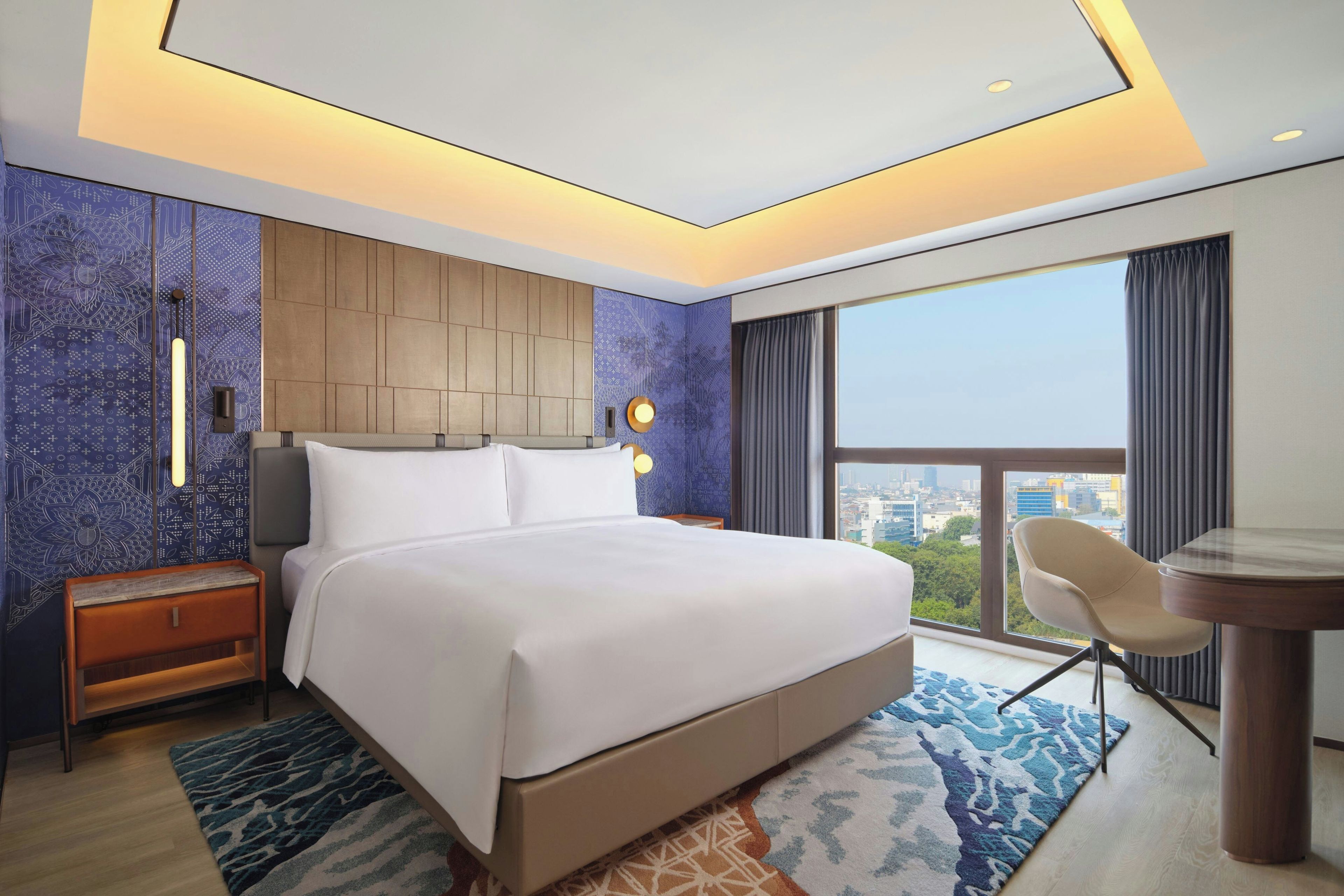 A modern hotel room with a large bed, a desk, and a view of the city.