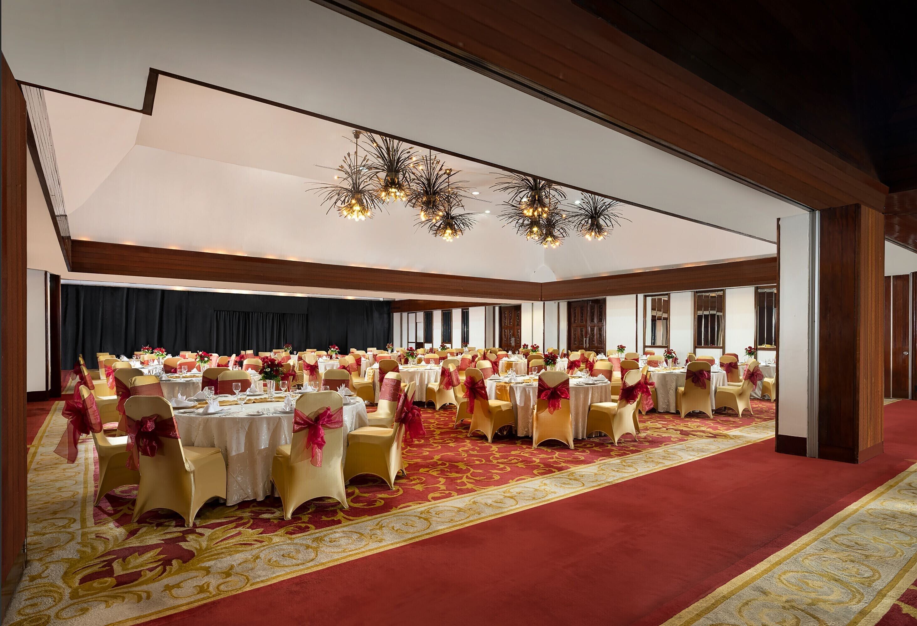 Un salón de banquetes con mesas redondas, sillas y alfombra roja.