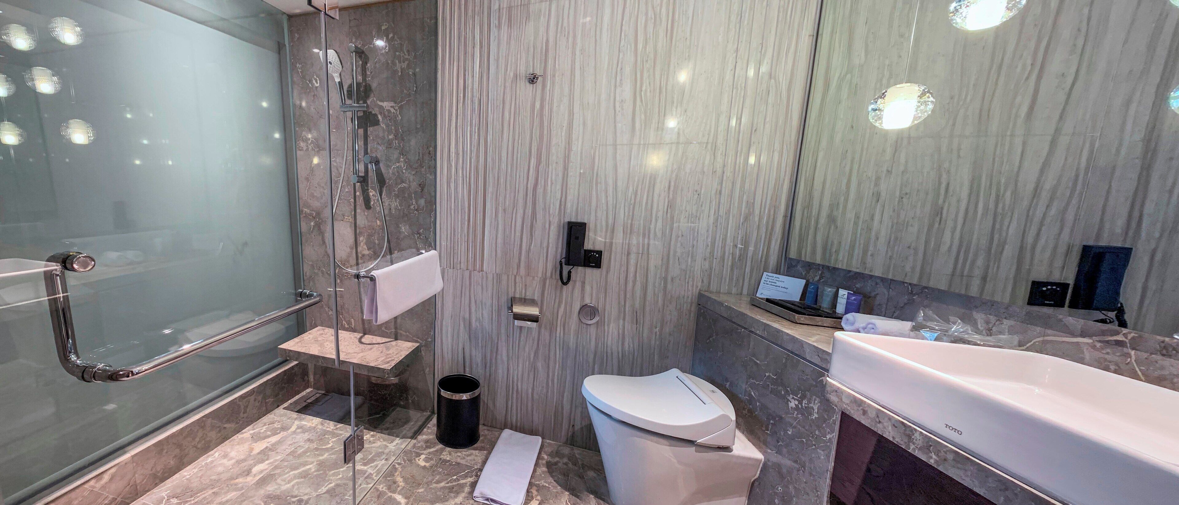 A modern bathroom with a glass-enclosed shower, a white toilet, and a large white bathtub.