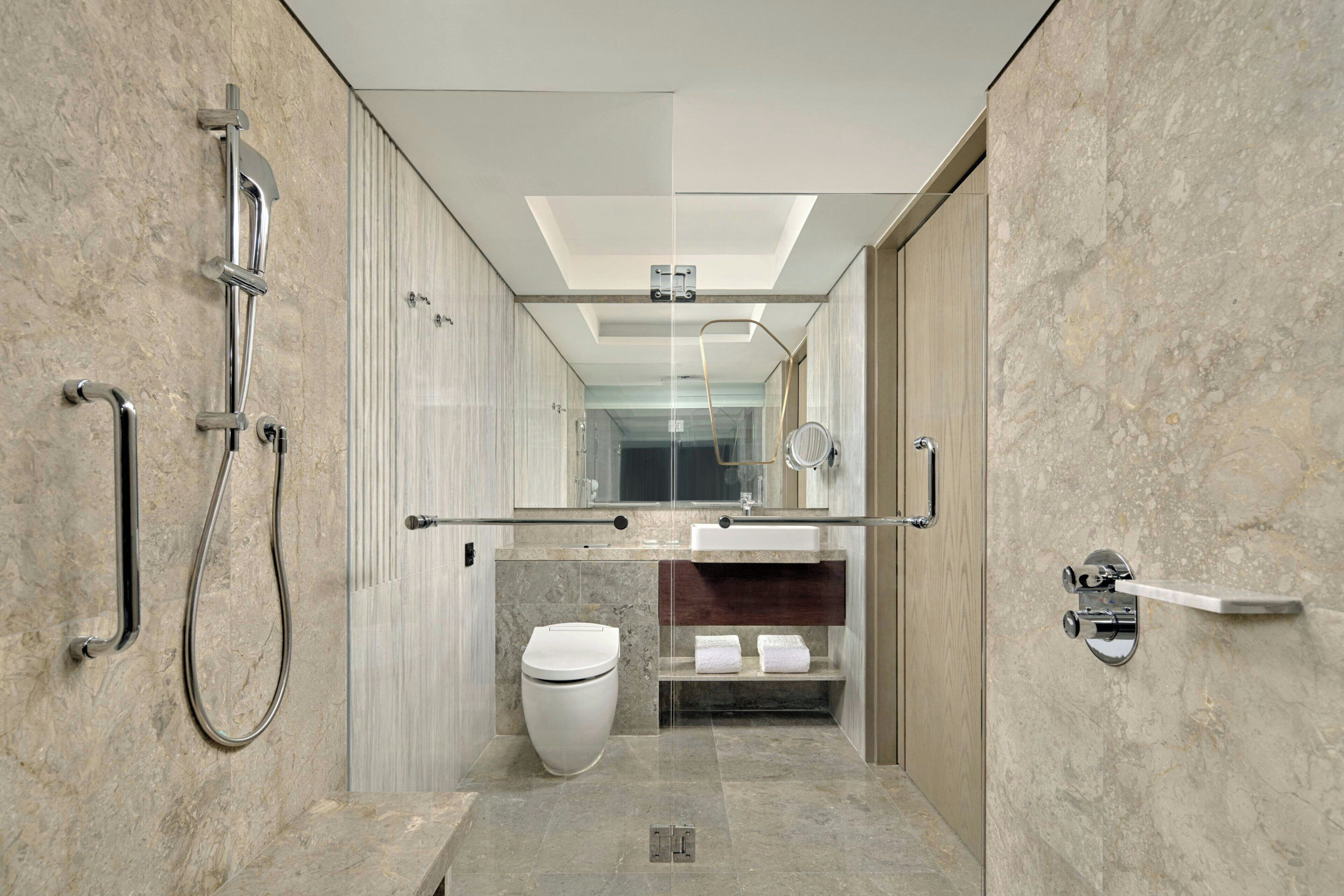 A modern bathroom with a shower, toilet, and sink, featuring marble walls and a glass enclosure.