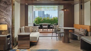 Ein modernes Wohnzimmer mit einer Couch, einem Couchtisch und einem Essbereich mit Stühlen. Ein großes Fenster bietet Blick auf Gebäude und Grünflächen.
