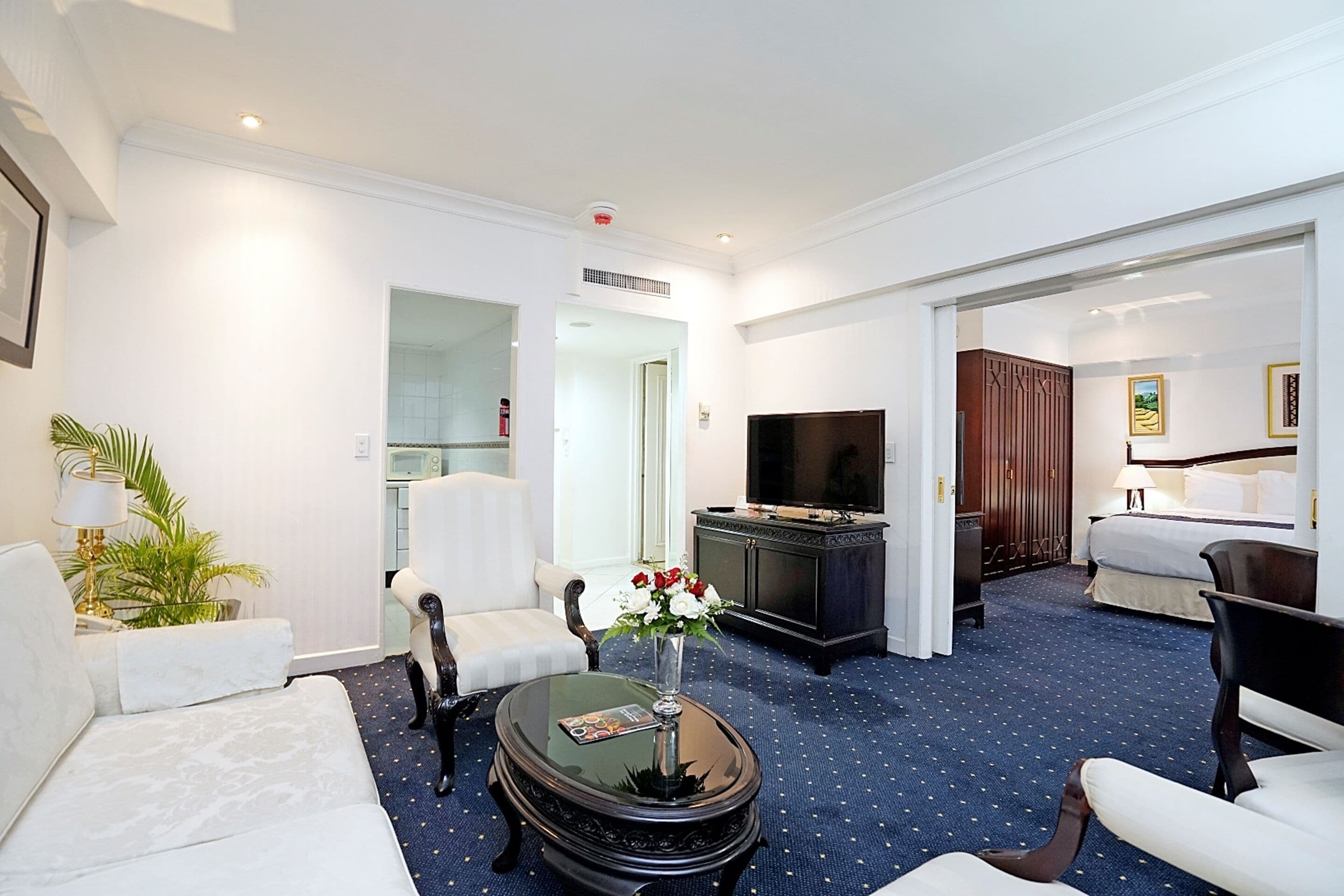 A hotel room with a living area featuring a sofa, armchairs, a coffee table, a TV, and a bed.