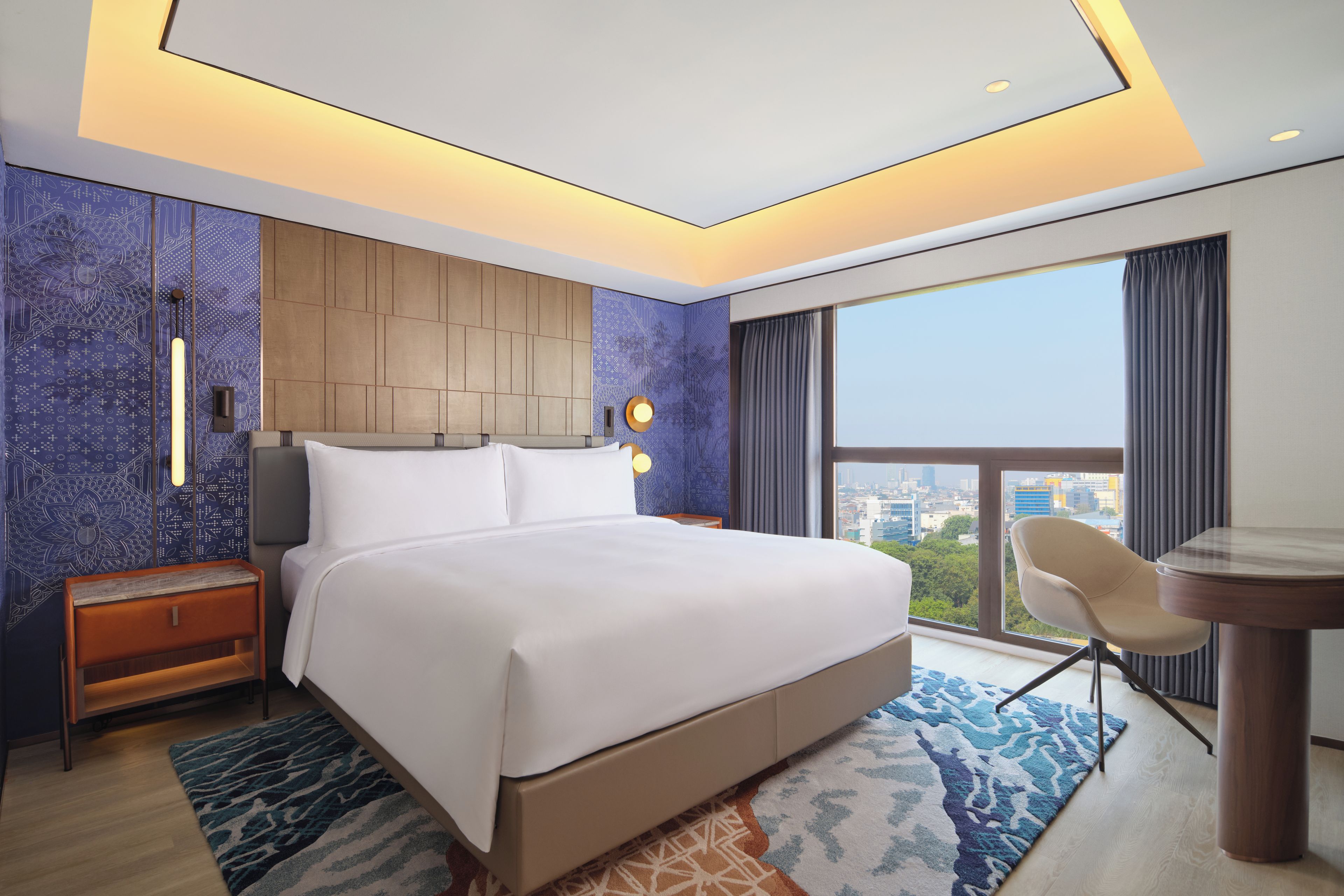 A hotel room with a large bed, a desk, and a view of the city.
