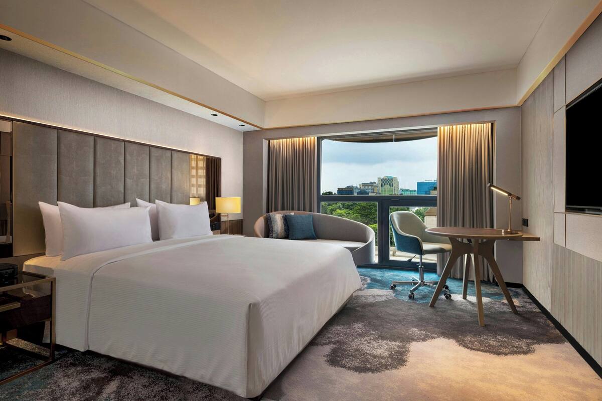 Quarto de hotel com uma cama grande, uma escrivaninha, uma cadeira e vista para a cidade.