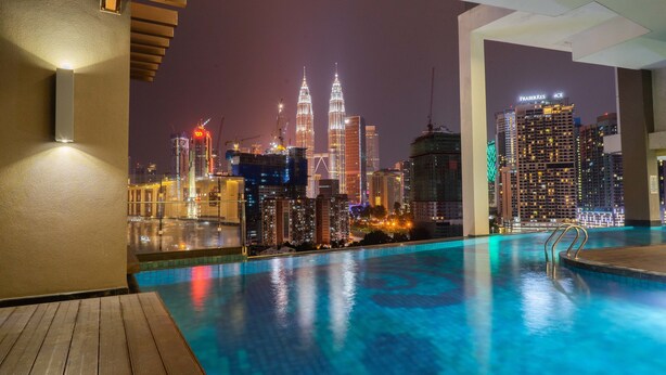 Vista nocturna de una zona de piscina con el horizonte de la ciudad al fondo, incluyendo las Torres Petronas.