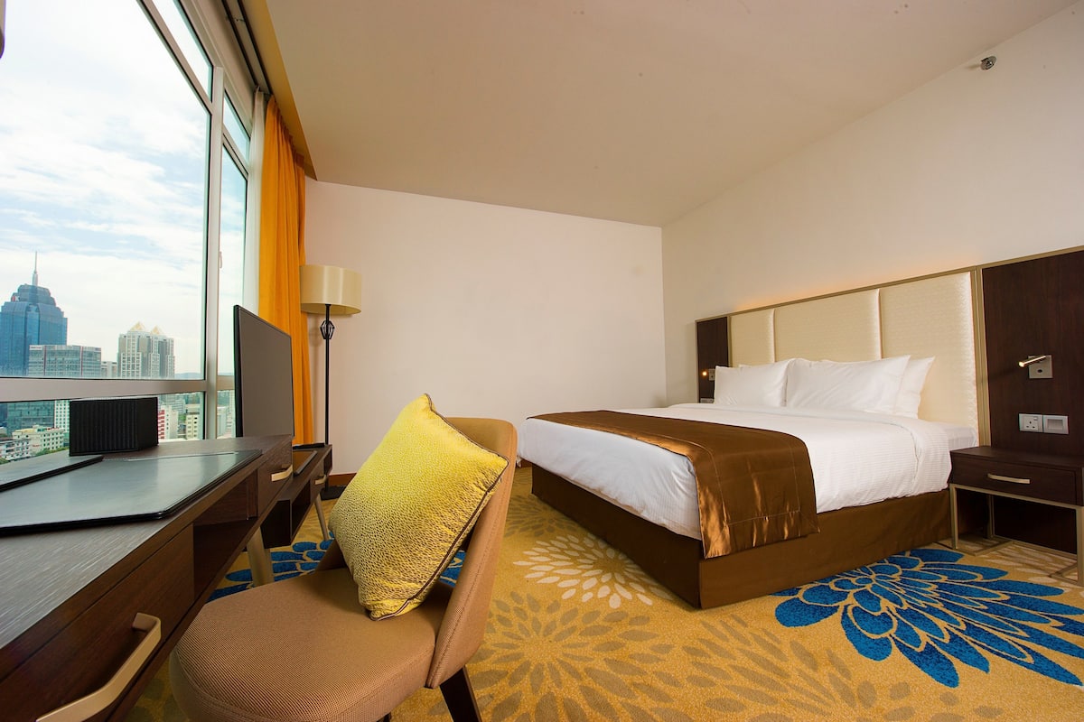 Een hotelkamer met een groot bed, een bureau met een computer, een stoel en uitzicht op de stad.