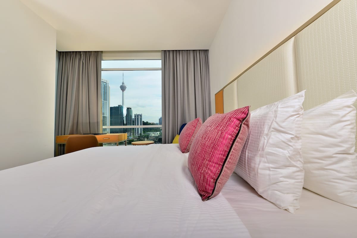 Een hotelkamer met een groot bed, een bureau en uitzicht op een stadsgezicht, inclusief een toren.