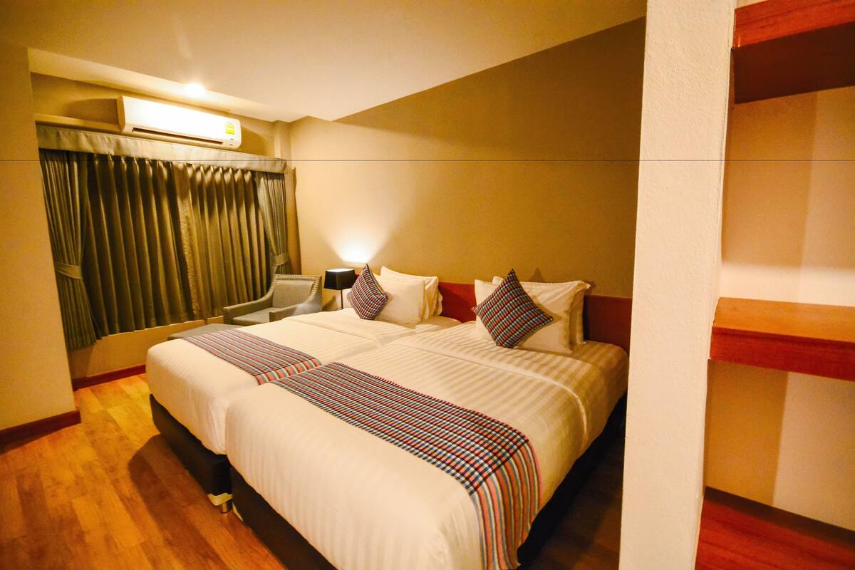 A hotel room with a large bed, a desk, an air conditioner, and a window with curtains.