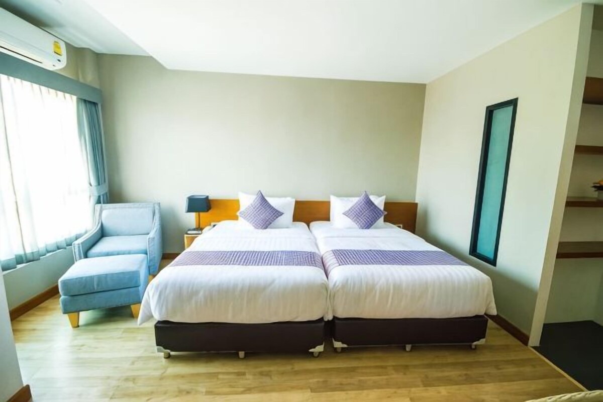 Habitación de hotel con dos camas, un sofá, una mesita de noche y un ventanal con cortinas.