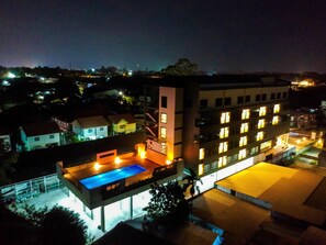 Un hotel de varios pisos con piscina en la azotea y fachada bien iluminada.