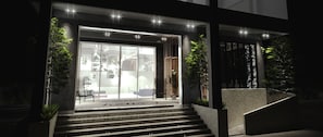 A modern building with a glass entrance, steps leading up to the door, and a staircase to the right.