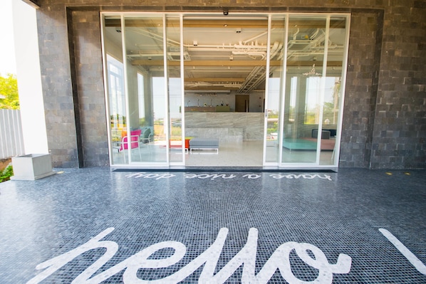 A modern building entrance with a glass door and a tiled floor with the word "hello" painted on it.
