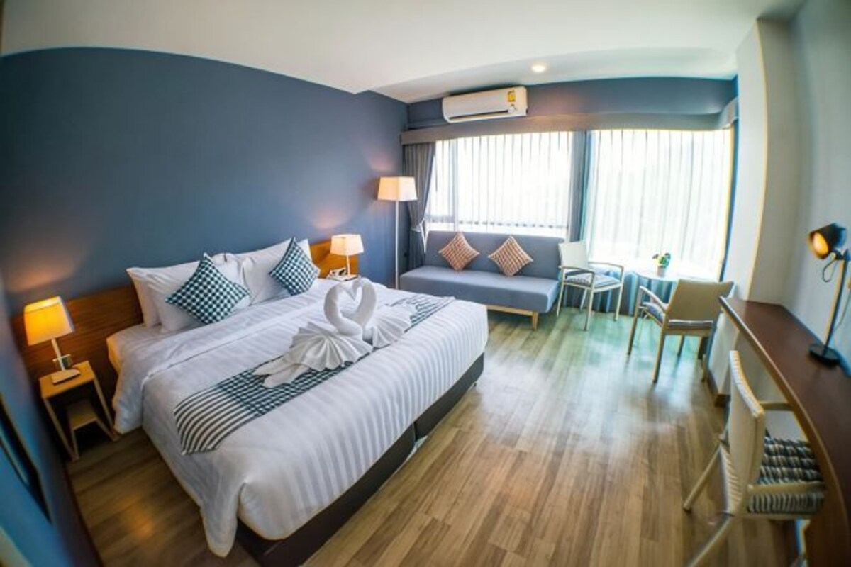 Habitación de hotel con cama, lámparas de noche, escritorio, silla, sofá y ventana con persianas.