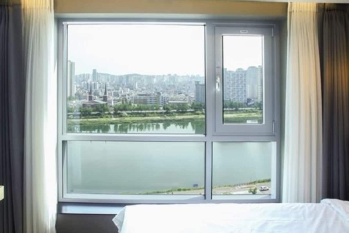 Habitació d'hotel amb una finestra gran que ofereix vistes a un paisatge urbà i una massa d'aigua.