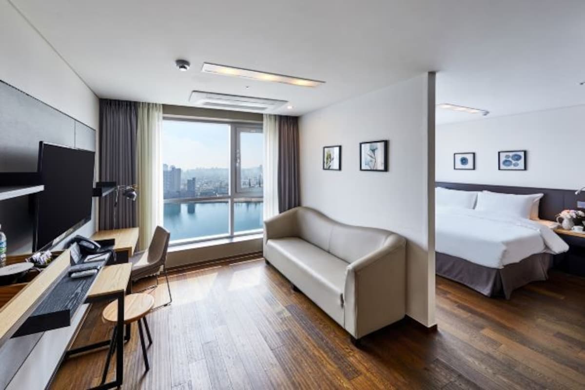 Habitació d'hotel moderna amb una finestra gran, un sofà, un llit, un escriptori i una televisió.