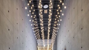 A hallway with a modern design, featuring a long corridor with a tiled floor, concrete walls, and a ceiling with hanging lights. - Hotel Riverside (Ulsan)