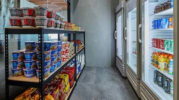 Un pasillo estrecho con estantes llenos de alimentos y bebidas, que conduce a una vitrina refrigerada.