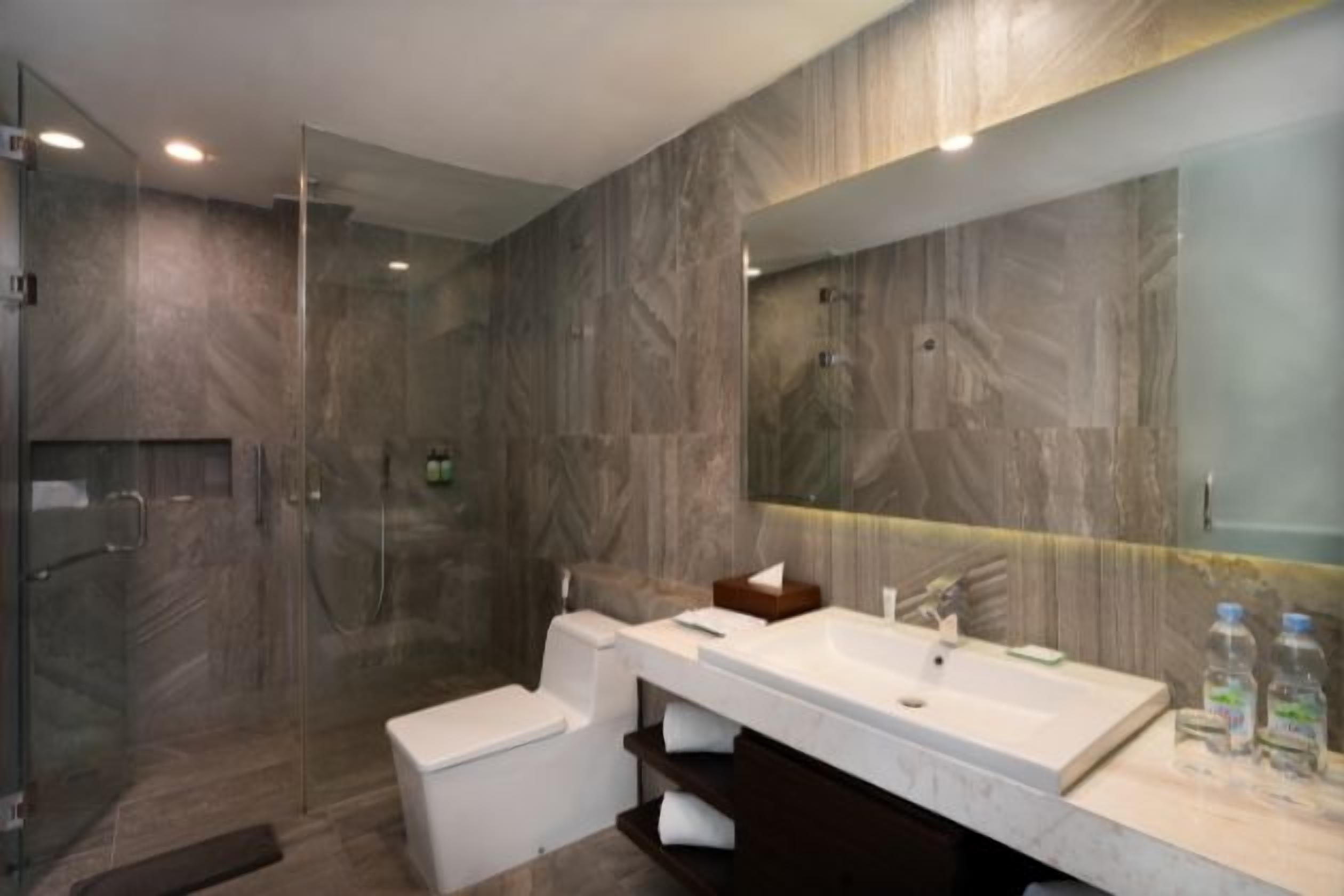 A modern bathroom with a glass-enclosed shower, a white toilet, a large sink with a mirror, and a vanity with a towel rack.