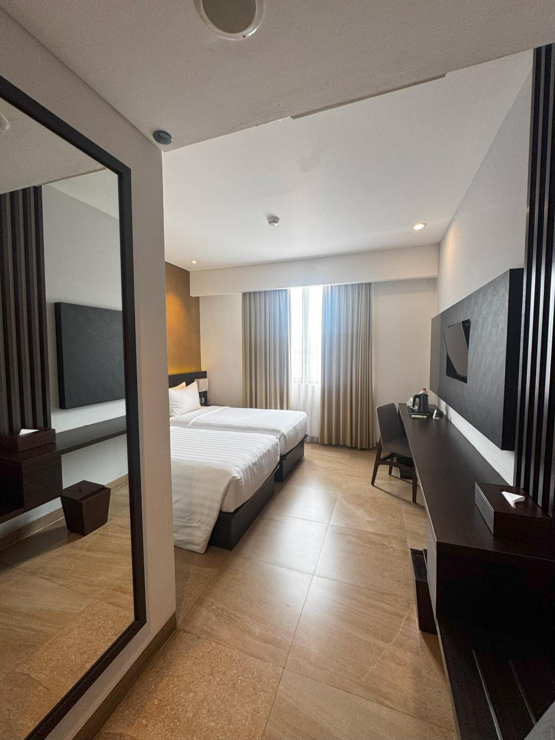 A hotel room with a large bed, a desk, a chair, a TV, and a mirror.
