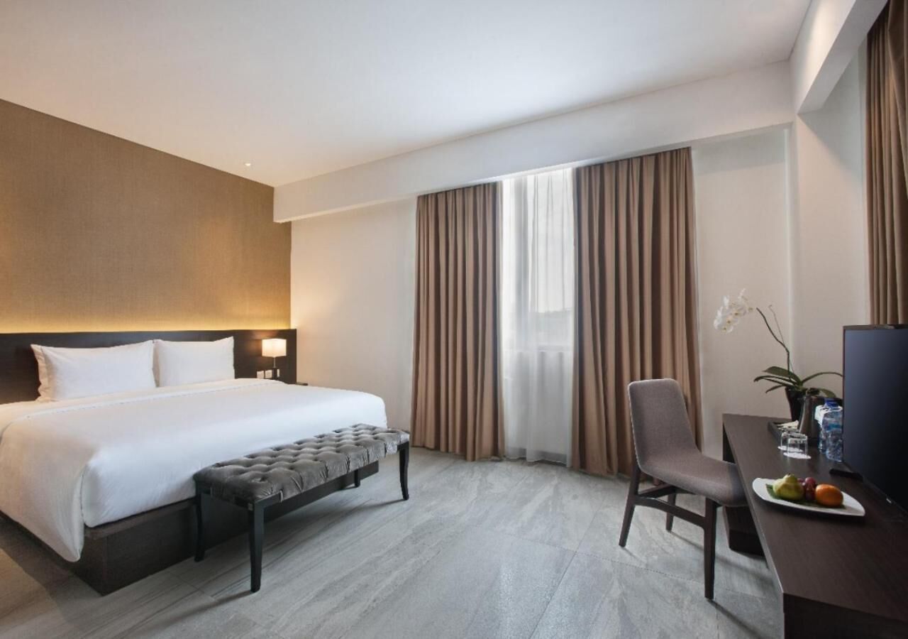 A hotel room with a bed, a desk with a chair, a television, and a window with curtains.