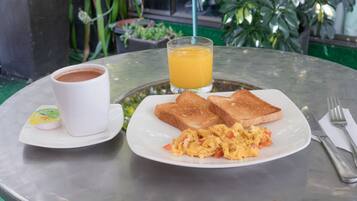 Un desayuno con tostadas, huevos revueltos, una taza de café y un vaso de jugo de naranja sobre una mesa redonda.