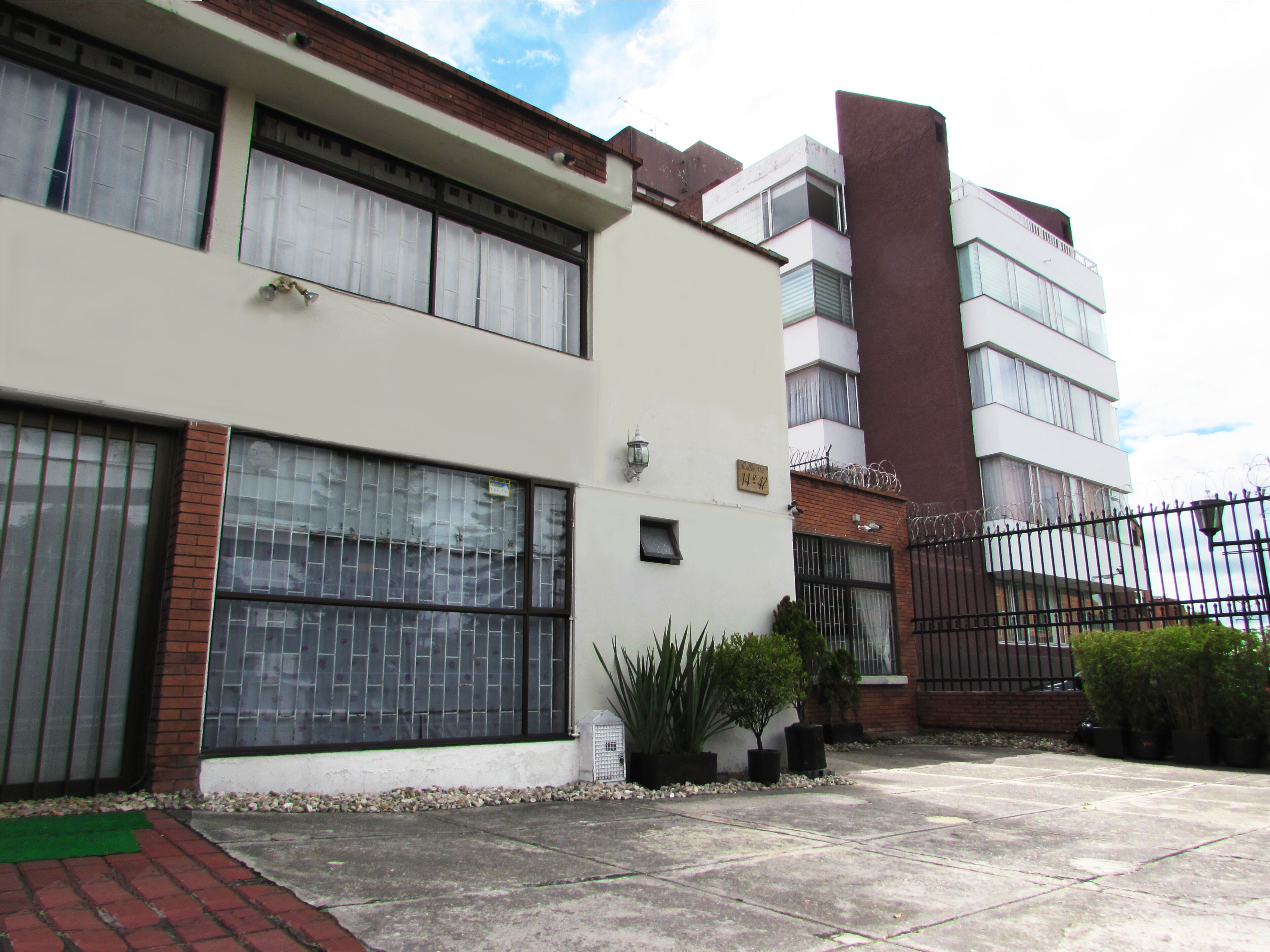 A two-story residential building with large windows, a brick facade, and a gated entrance.