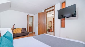 A bedroom with a bed, a sofa, a TV mounted on the wall, and a door leading to another room. - Hotel Calle 112 (Bogotá)