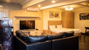 A modern hotel room with a bed, a TV, a refrigerator, a sofa, and a painting on the wall. - Classic Serviced Apartments (Lalitpur)