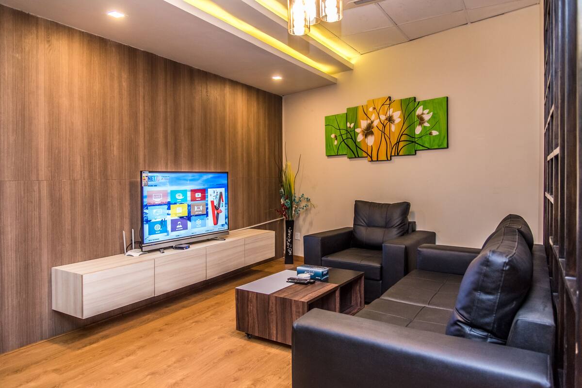Una sala de estar moderna con un televisor de pantalla plana, un mueble de madera para entretenimiento, una mesa de centro y un sofá.