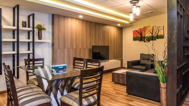 A modern living room with a glass dining table, wooden chairs, a sofa, and a flat-screen TV. - Classic Serviced Apartments (Lalitpur)