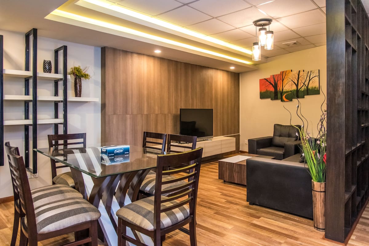 Una sala de estar moderna con una mesa de comedor de vidrio, sillas de madera, un sofá y un televisor de pantalla plana.
