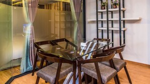 A glass-top dining table with wooden chairs, a glass partition, and a black metal shelf with potted plants. - Classic Serviced Apartments (Lalitpur)