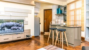 A modern kitchen with a central island, wooden flooring, and a television displaying a nature scene. - Classic Serviced Apartments (Lalitpur)