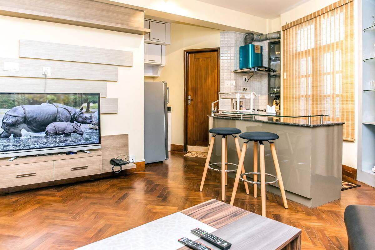 Una cocina moderna con una isla central, suelo de madera y un televisor mostrando una escena de la naturaleza.