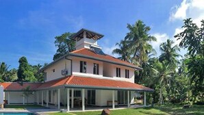 A symmetrical building with a red-tiled roof, a central pool, and a lush green landscape with palm trees.
