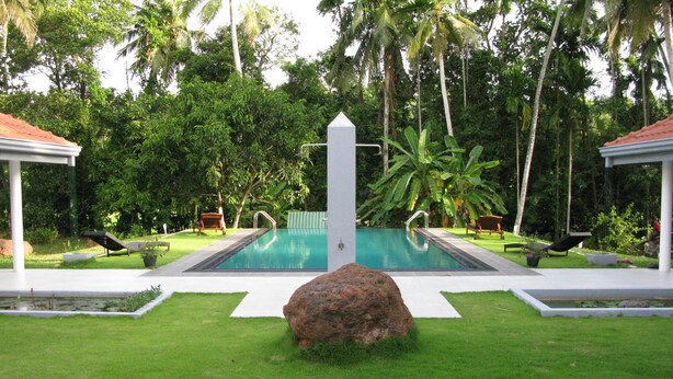 A rectangular swimming pool with a central pole, surrounded by a well-maintained lawn and palm trees.