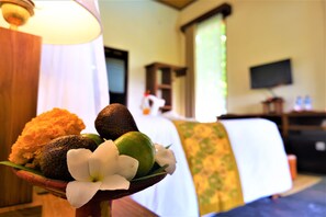 A bed with a white and green patterned bedspread, a flat-screen TV on a wooden stand, and a wooden nightstand with a lamp. - Swar Bali Lodge (Munduk)