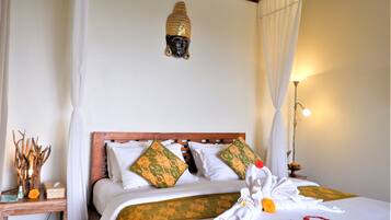 A neatly made bed with white and patterned pillows, a wooden headboard, and a decorative Buddha head above it.